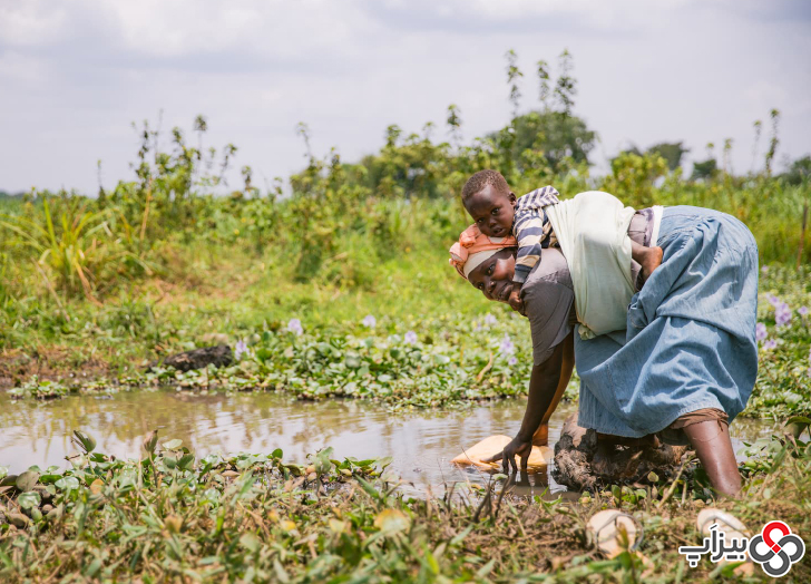  زنی به همراه فرزندش که از باتلاق روستای کیکومرا بیری آب جمع آوری می‌ کند